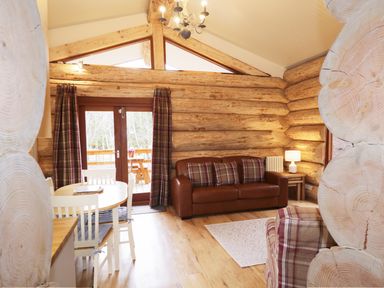 A living room with a brown leather sofa and plaid cushions next to a dining table with white chairs in a log cabin at Moorhen Lodge in North Kessock