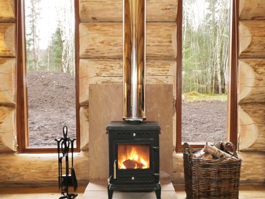 A wood burning stove with fire inside between two tall windows in a log cabin at Moorhen Lodge in North Kessock