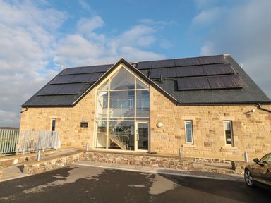 A stone building with large glass entrance and solar panels on the roof at St  Cruz in Embleton