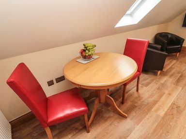 A wooden round table with a bowl of fruit and two red chairs in a room with wood flooring and a skylight window at St Cruz in Embleton