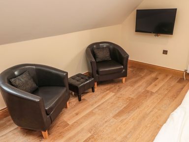 Two black armchairs with cushions and a small black ottoman on a wooden floor facing a wall-mounted flat screen TV at St Cruz in Embleton