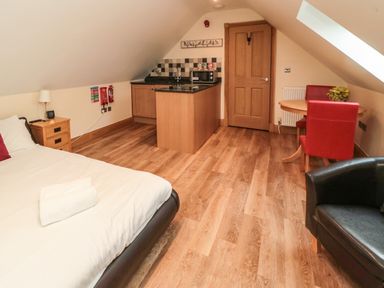 A bedroom with a bed side table bed kitchen island and small round dining table with red chairs at St Cruz in Embleton