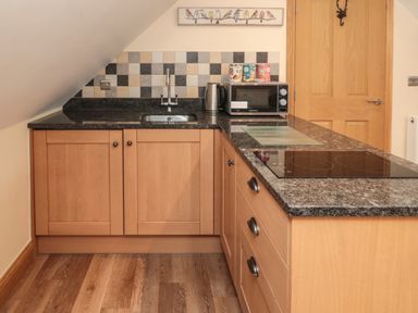 A kitchen with wooden cabinets a black countertop a sink a microwave kettle and a stovetop at St. Cruz in Embleton