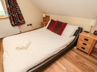 A bedroom with a double bed with white sheets and pillows two bedside tables with lamps and a window with patterned curtains at St  Cruz in Embleton
