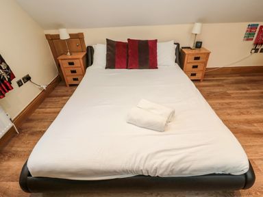 A bedroom with a double bed with white linens and towels on top two bedside tables with lamps hardwood floor at St Cruz in Embleton