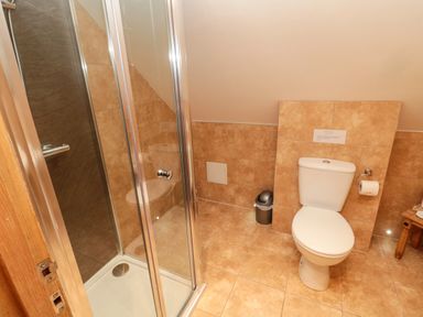A bathroom with a shower enclosure a toilet a small trash bin and a wooden stool at St Cruz in Embleton