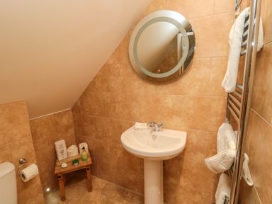 A small bathroom with a pedestal sink round mirror wooden stool with toiletries and towels on a heated towel rail at St Cruz in Embleton