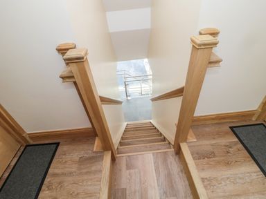 A wooden staircase with handrails leading down from a wooden floor hallway at St Cruz in Embleton