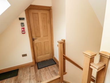 A wooden door at the top of a staircase with wooden railings and light-colored walls at St Cruz in Embleton