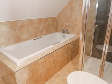 A bathroom with a bathtub, shower enclosure, and tiled walls and floor at Newton View in Embleton