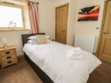 A bedroom with a single bed bedside table lamp towels on bed and striped curtains at Newton View in Embleton