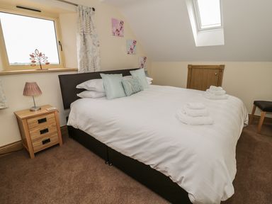 A bedroom with a large bed with white bedding and pillows beside a window and a wooden nightstand at Newton View in Embleton