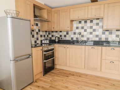 A kitchen with wooden cabinets a stainless steel refrigerator an oven a kettle and a checkered tile backsplash at Newton View in Embleton