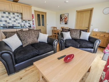 A living area with two black sofas and a wooden coffee table with a red bowl and remote at Newton View in Embleton