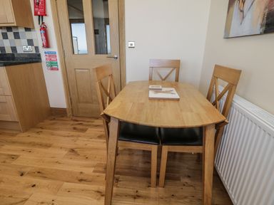 A wooden dining table with three chairs in a kitchen next to a white radiator and wooden door at Newton View in Embleton