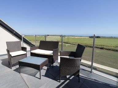 A balcony with outdoor wicker furniture and glass railing overlooking fields at Newton View in Embleton