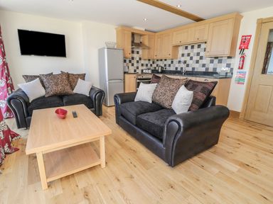 A living room with two black sofas and a wooden table in front of a kitchen with wooden cabinets and a silver refrigerator at Newton View in Embleton