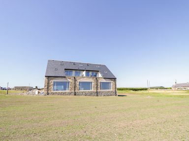 A stone house with large windows on a grassy field under a clear sky at Newton View in Embleton