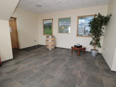 An empty room with gray tile floor a wooden barrel a small wooden table with a black box a potted plant and two framed pictures on the wall at Newton View in Embleton