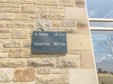 A stone wall with a black plaque listing St Dolmen St Cruz Newton View and Mill View at Newton View in Embleton