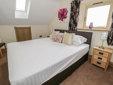 A bedroom with a double bed pillows bedside table window and skylight at Mill View in Embleton