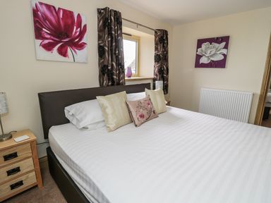 A bedroom with a double bed cushions bedside tables and paintings on the walls at Mill View in Embleton