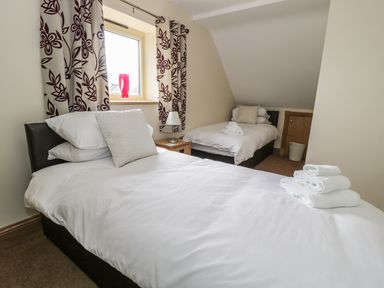 A bedroom with two single beds white bedding floral curtains and a window at Mill View in Embleton