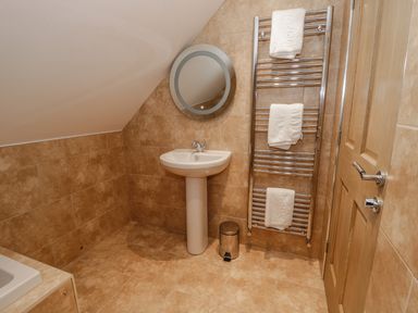 A bathroom with a pedestal sink a round mirror a towel rack with towels a trash can and a wooden door at Mill View in Embleton