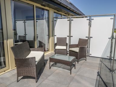An outdoor balcony with wicker furniture and a glass top table at Mill View in Embleton