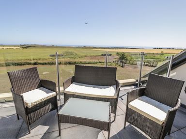 An outdoor seating area with two armchairs a loveseat and a glass-top table on a balcony with a view of fields at Mill View in Embleton
