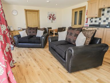 A seating area with two black sofas and cushions in an open living space with wooden flooring at Mill View in Embleton
