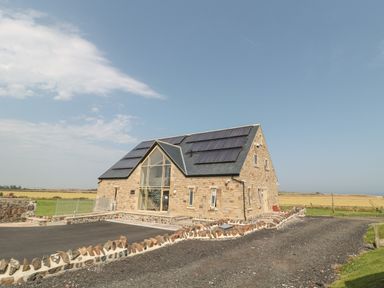 A stone building with solar panels on the roof and large glass windows in a rural area at Mill View in Embleton