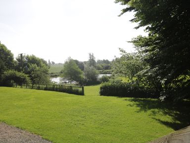A grassy yard with trees and a small pond in the background at Apple Tree Lodge in Gillingham