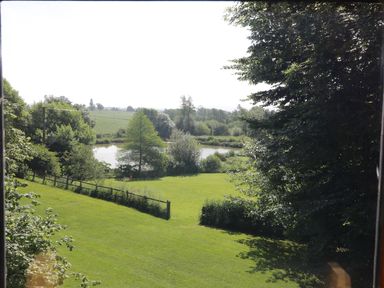 A grassy yard with a wooden fence and a small pond surrounded by trees at Apple Tree Lodge in Gillingham