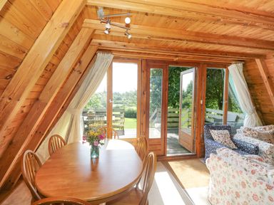 A wooden interior room with a dining table and chairs and a seating area with sofas near glass doors leading outside at Apple Tree Lodge in Gillingham