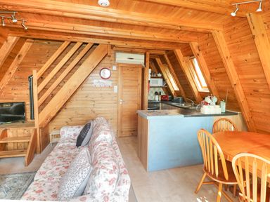 A wooden cabin interior with a floral sofa a small dining table with chairs a kitchen counter and skylight windows at Apple Tree Lodge in Gillingham