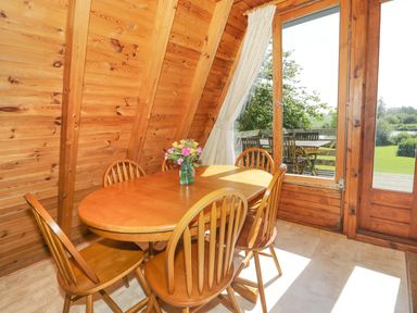 A dining area with a wooden table and chairs next to large windows overlooking a garden at Apple Tree Lodge in Gillingham