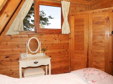 A wooden bedroom with a white dressing table and mirror under a window with curtains at Apple Tree Lodge in Gillingham