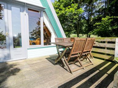 A wooden outdoor dining table and chairs on a deck next to a building with glass doors and windows at Apple Tree Lodge in Gillingham