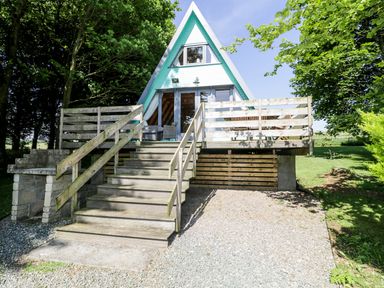 An a-frame cabin with wooden stairs and railing leading to a raised deck surrounded by trees at Apple Tree Lodge in Gillingham