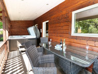 An outdoor covered patio with wicker chairs a glass table a hot tub and wooden walls at Kipling Lodge in Rudyard