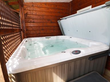 A hot tub with bubbling water inside a wooden enclosure at Kipling Lodge in Rudyard