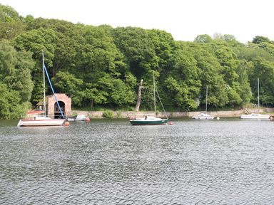 A body of water with sailboats and a small boathouse near a wooded shoreline at Kipling Lodge in Rudyard