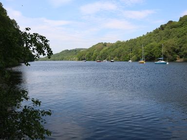 A river with several boats moored along the tree-lined banks at Kipling Lodge in Rudyard