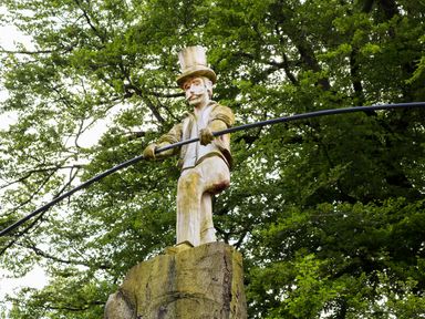 A wooden statue of a man with a top hat holding a long pole in a forest at Kipling Lodge in Rudyard