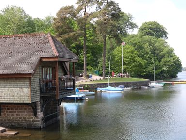 A boathouse on a river with boats moored near a grassy area with trees and a flagpole at Kipling Lodge in Rudyard
