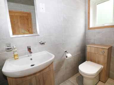 A bathroom with a sink and mirror next to a toilet under a window at Kipling Lodge in Rudyard