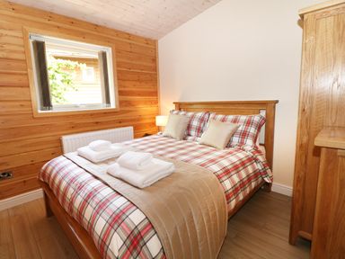 A bedroom with a wooden bed with plaid bedding and folded towels at Kipling Lodge in Rudyard