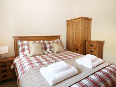 A bedroom with a bed with plaid bedding two white towel sets bedside tables and a wooden wardrobe at Kipling Lodge in Rudyard
