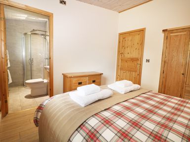 A bedroom with a bed with towels on it wooden furniture and an ensuite bathroom at Kipling Lodge in Rudyard